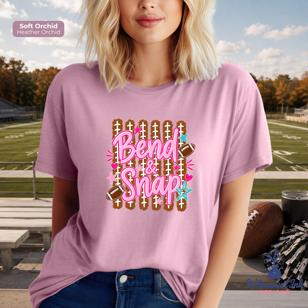 A woman wearing a light pink graphic t-shirt with a 'Bend & Snap' football theme, set against an outdoor football field background.