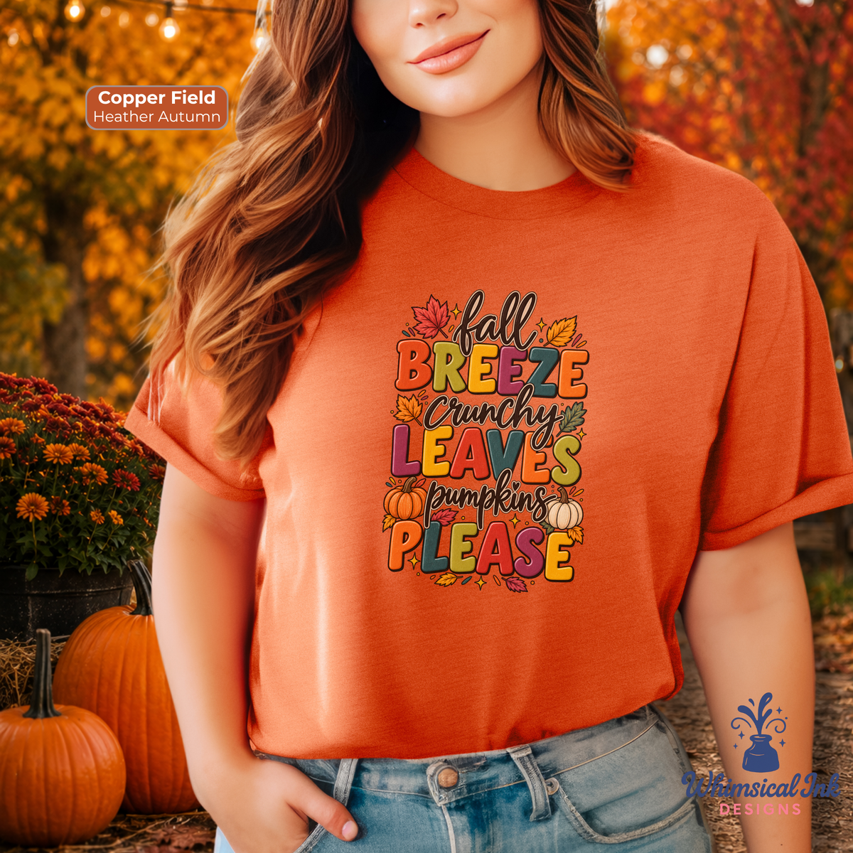 A woman wearing a copper-orange graphic t-shirt with a colorful autumn-themed text design that reads 'Fall Breeze Crunchy Leaves Pumpkins PLEASE'. The background depicts an outdoor fall scene with pumpkins, mums, and autumn foliage.