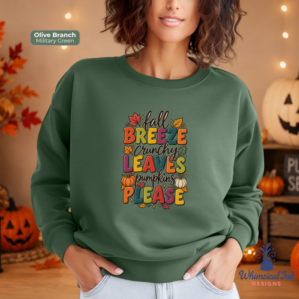 A woman wearing an olive branch military green sweatshirt with a colorful autumn-themed graphic that reads 'fall Breeze crunchy leaves pumpkins please' in orange, yellow, and red letters. The background is a cozy, warm-toned Halloween setting with pumpkins and string lights.