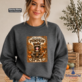 A woman wearing a dark heather gray crewneck sweatshirt with a 'feeling PUMPKIN SPICY' autumn raccoon graphic. The sweatshirt is labeled as 'Stormy Blend' and features a 'Whimsical Ink' brand logo in the bottom right corner, set against a cozy indoor background with pumpkins and a plant.