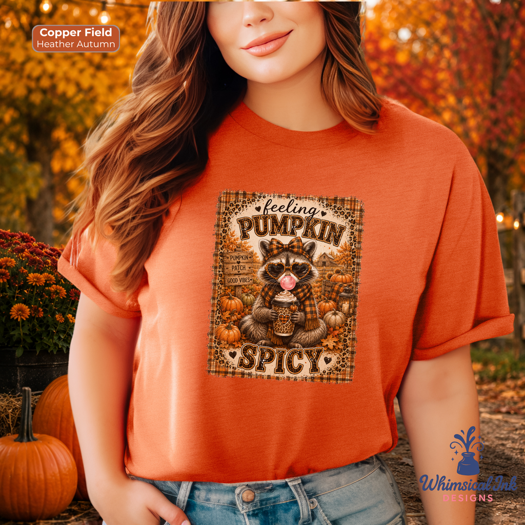 A woman wearing a burnt orange graphic t-shirt with a fall turkey design that reads 'feeling PUMPKIN SPICY'. The background is a blurred autumn outdoor scene with pumpkins and fall foliage.