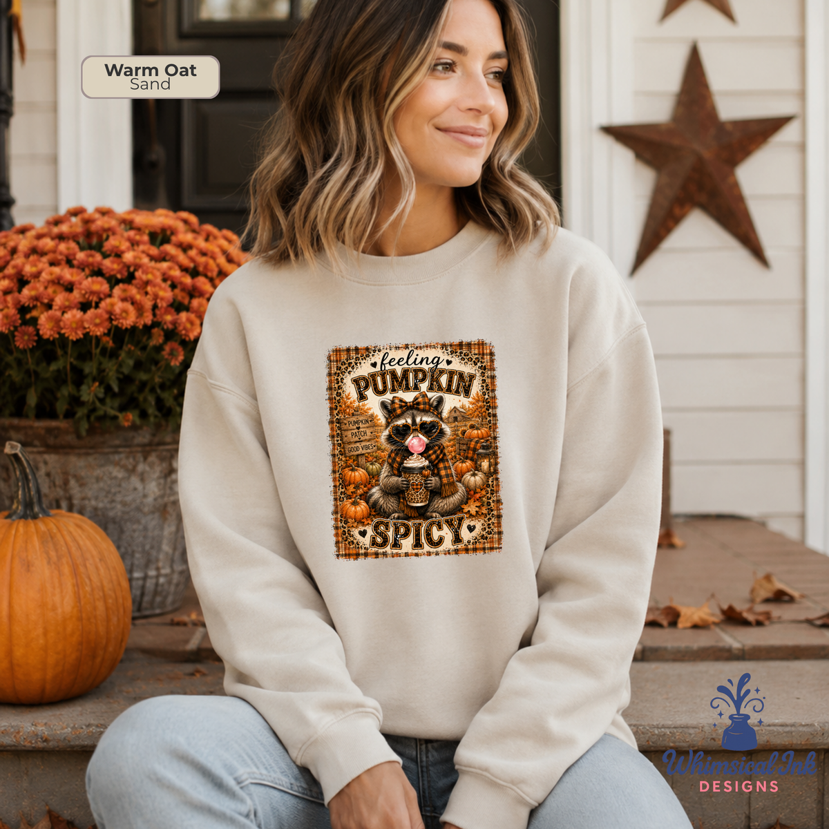 A woman wearing a cream-colored sweatshirt with a 'feeling PUMPKIN SPICY' cartoon raccoon graphic, sitting on a porch with a pumpkin and orange flowers in the background.