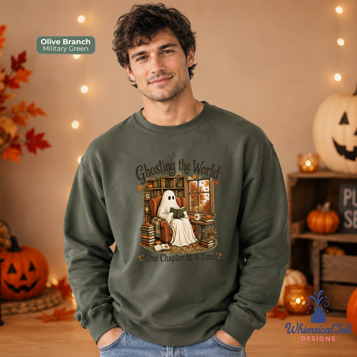 A man wearing an olive branch crewneck sweatshirt with a Halloween graphic of a ghost sitting in a chair reading a book. The sweatshirt has a text overlay that reads 'Ghosting the World One Chapter at a Time' and a color label indicating 'Olive Branch Military Green'.