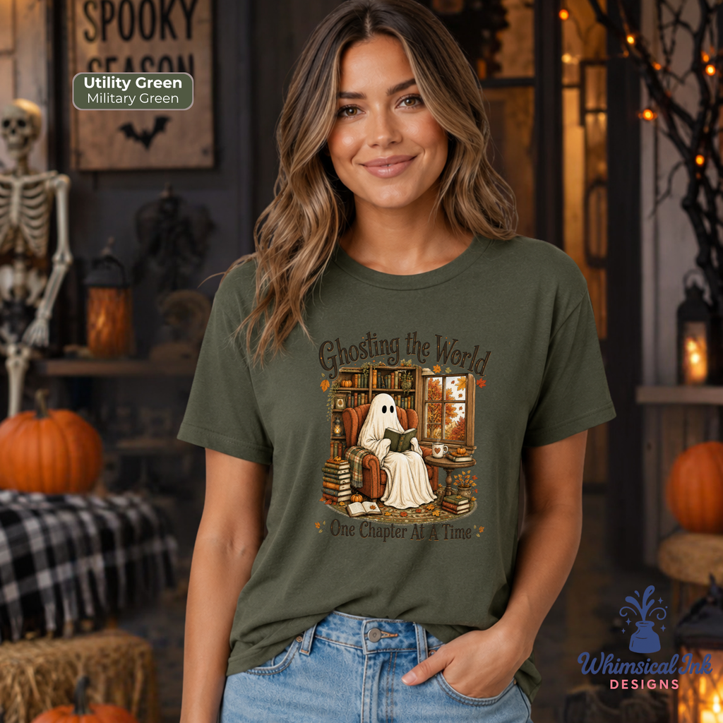 A woman wearing a military green graphic t-shirt with a ghost-themed illustration and the text 'Ghosting the World One Chapter At A Time'. The background is a cozy, decorated Halloween scene with pumpkins, a skeleton, and warm lighting.