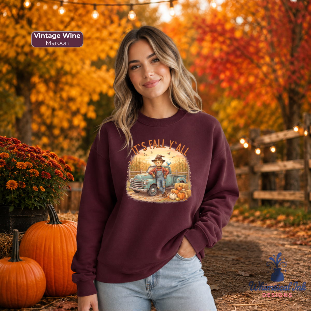A woman wearing a maroon crewneck sweatshirt with a vintage autumn graphic, standing outdoors in a fall-themed setting with pumpkins and orange foliage.