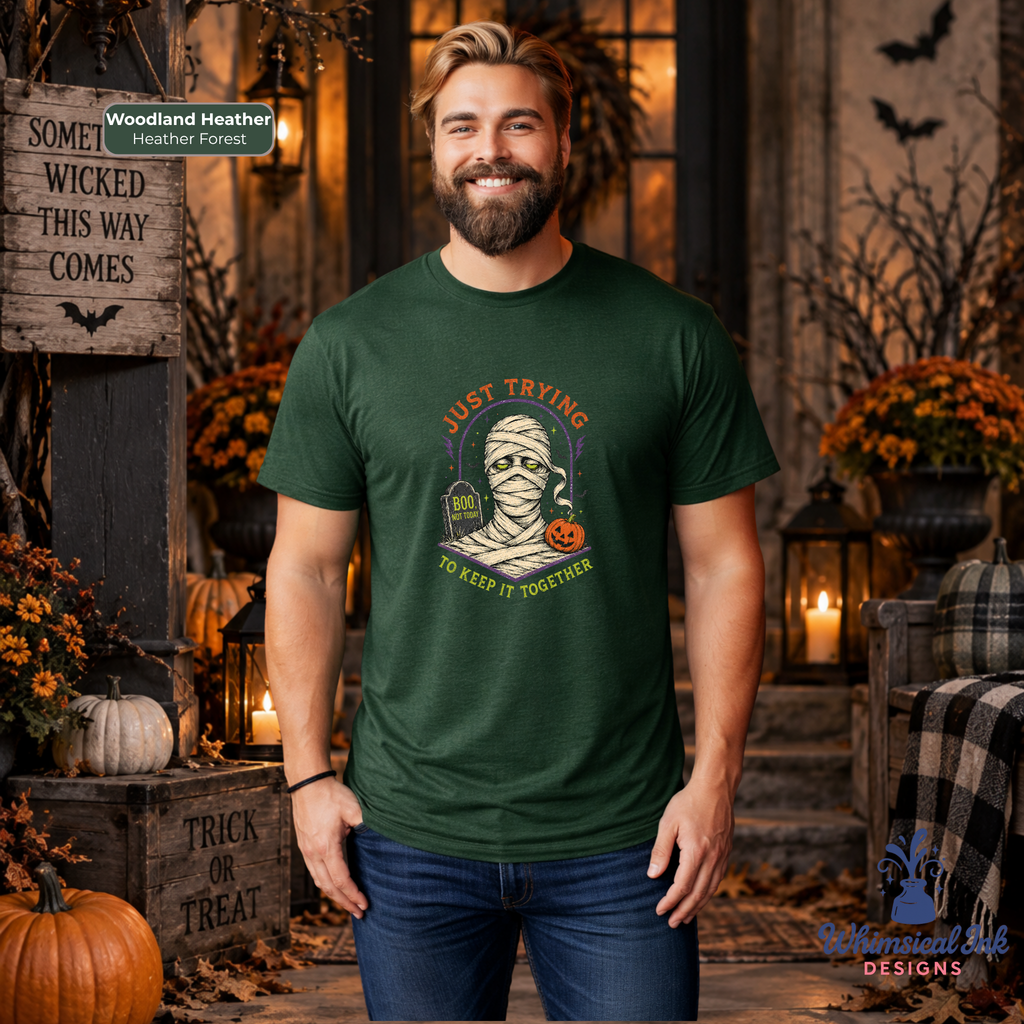 A man wearing a dark green graphic t-shirt with a Halloween mummy design, standing in a cozy, decorated autumnal porch setting with pumpkins, candles, and fall foliage.