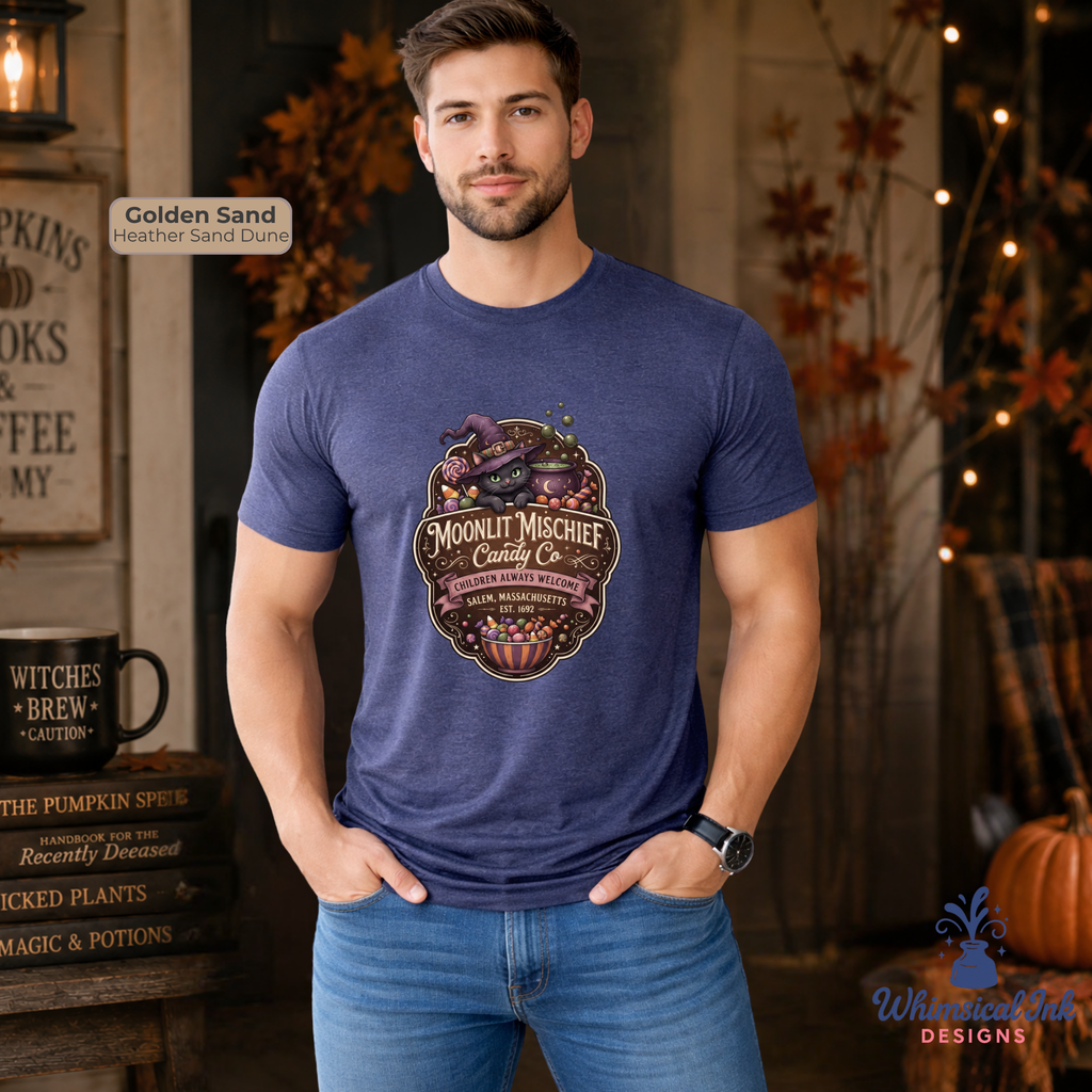 A man wearing a heathered blue crewneck t-shirt with a detailed graphic print of a witch's cauldron and the text 'Moonlit Mischief Candy Co'. The background depicts a cozy, autumn-themed rustic room with warm lighting, wooden decor, and a pumpkin.