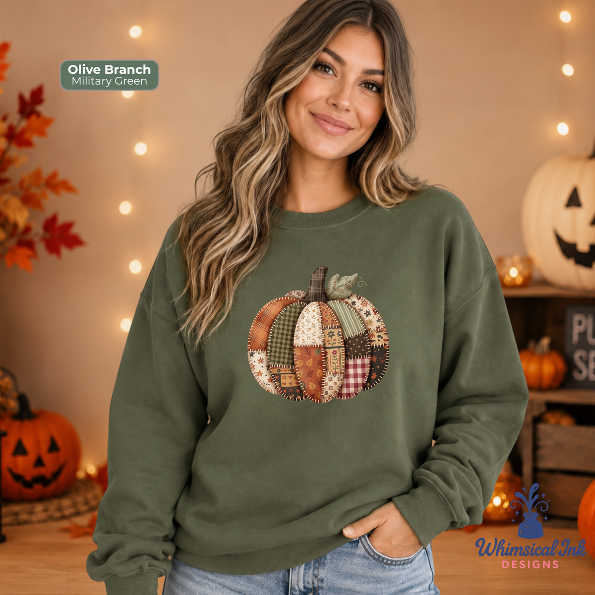 A woman wearing an olive branch sweatshirt with a patchwork pumpkin design on the front, posed in a cozy autumn-themed room with string lights and pumpkins.