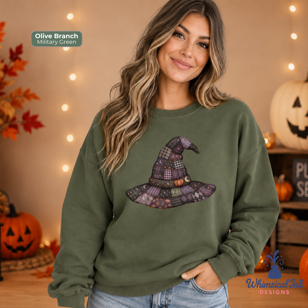 A woman wearing an olive branch sweatshirt with a plaid witch hat graphic, posed in a cozy, warmly lit autumn setting with pumpkins and fairy lights. The text 'Olive Branch Military Green' is visible in the top left, and the 'Whimsical Ink DESIGNS' logo is in the bottom right.