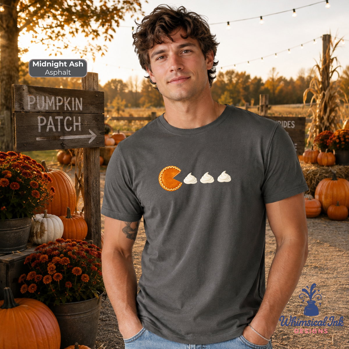 A man wearing a dark gray graphic t-shirt with a pumpkin patch design, standing in an outdoor autumn pumpkin patch setting at sunset. The shirt features an orange pie character and three white whipped cream shapes.
