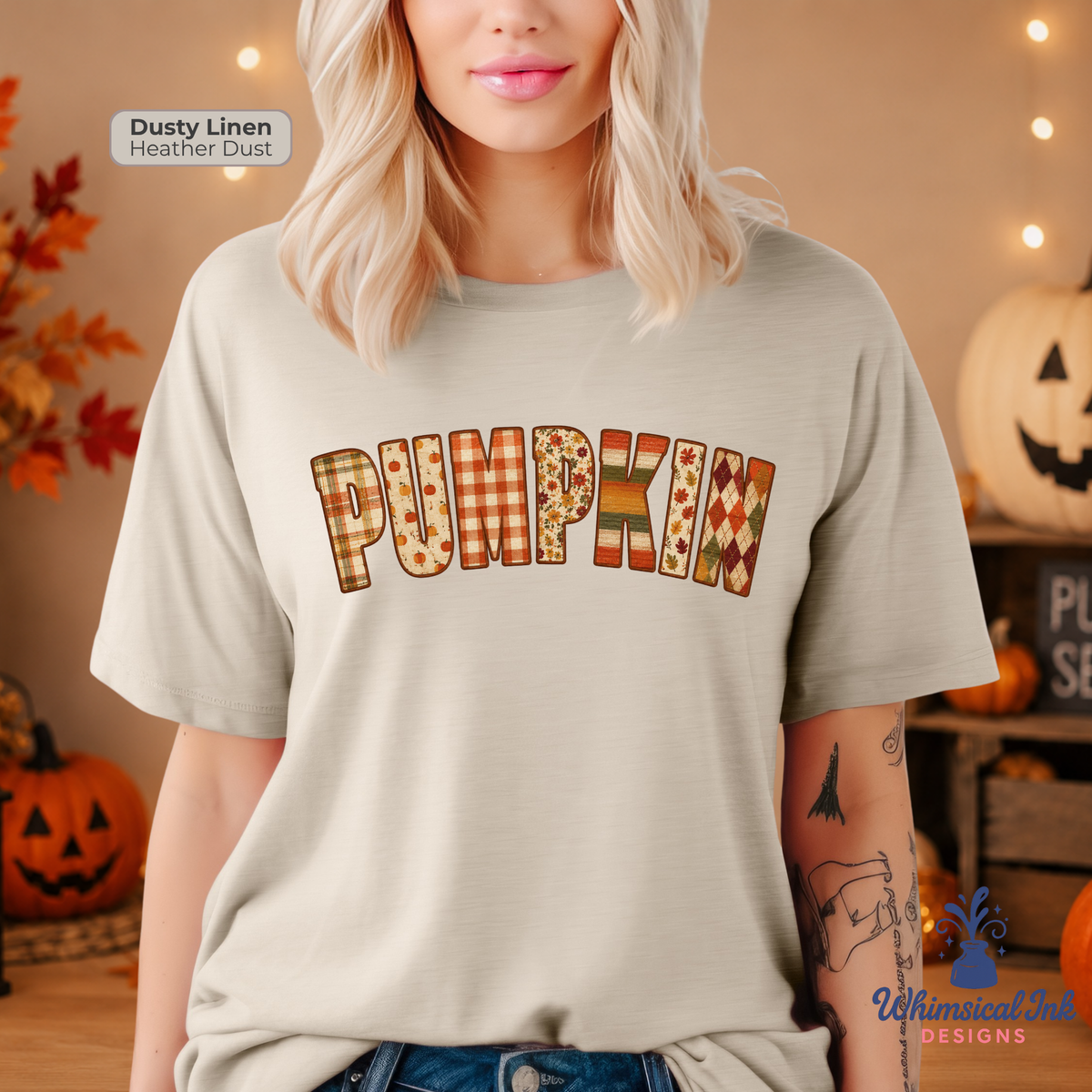 A woman wearing a light beige t-shirt with 'PUMPKIN' written across the chest in a patchwork autumn pattern of orange, brown, and yellow. The background is a cozy, warm-toned fall setting with pumpkins and string lights.