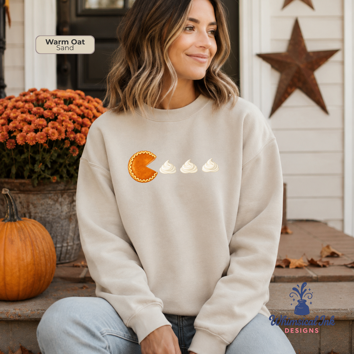 A woman wearing a cream sweatshirt with a graphic of a pumpkin pie slice and three whipped cream dollops on the front. The text 'Warm Oat Sand' is visible in the top left corner.