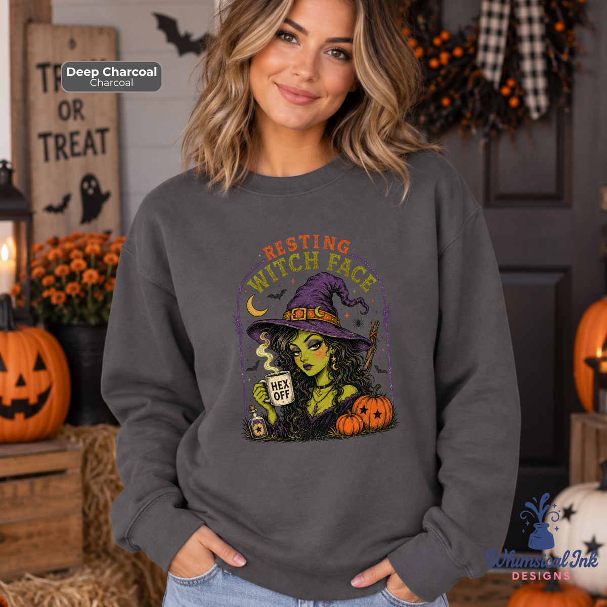 A woman wearing a dark charcoal gray sweatshirt with a colorful graphic of a witch holding a potion next to pumpkins and the text 'RESTING WITCH FACE'. The background is a cozy, decorated Halloween scene with pumpkins, a jack-o'-lantern, and a 'TRICK OR TREAT' sign.