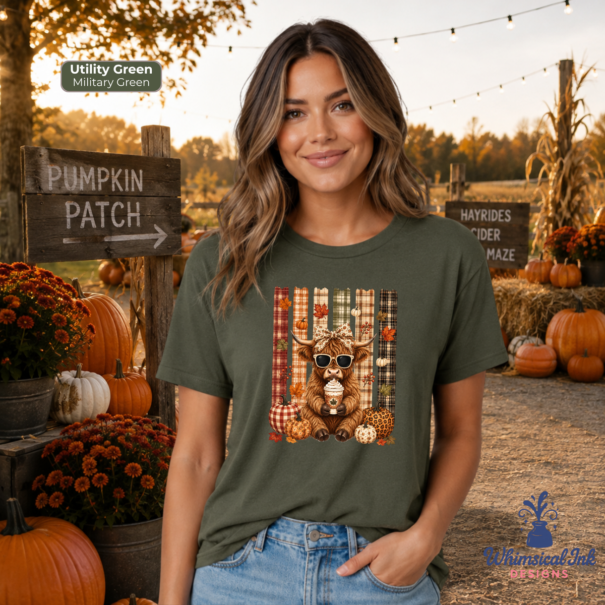 A woman wearing an olive green graphic t-shirt with a fall-themed deer print, standing in a pumpkin patch setting. The t-shirt features a graphic of a deer wearing sunglasses in front of a plaid background with pumpkins and autumn decorations.