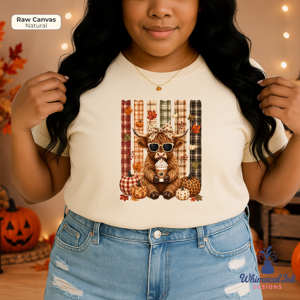 A woman wearing a cream-colored t-shirt with a graphic of a cute brown Scottish highland cow wearing sunglasses, surrounded by autumn elements like pumpkins, plaid stripes, and maple leaves. The background is a warm, cozy fall scene with string lights and pumpkins.