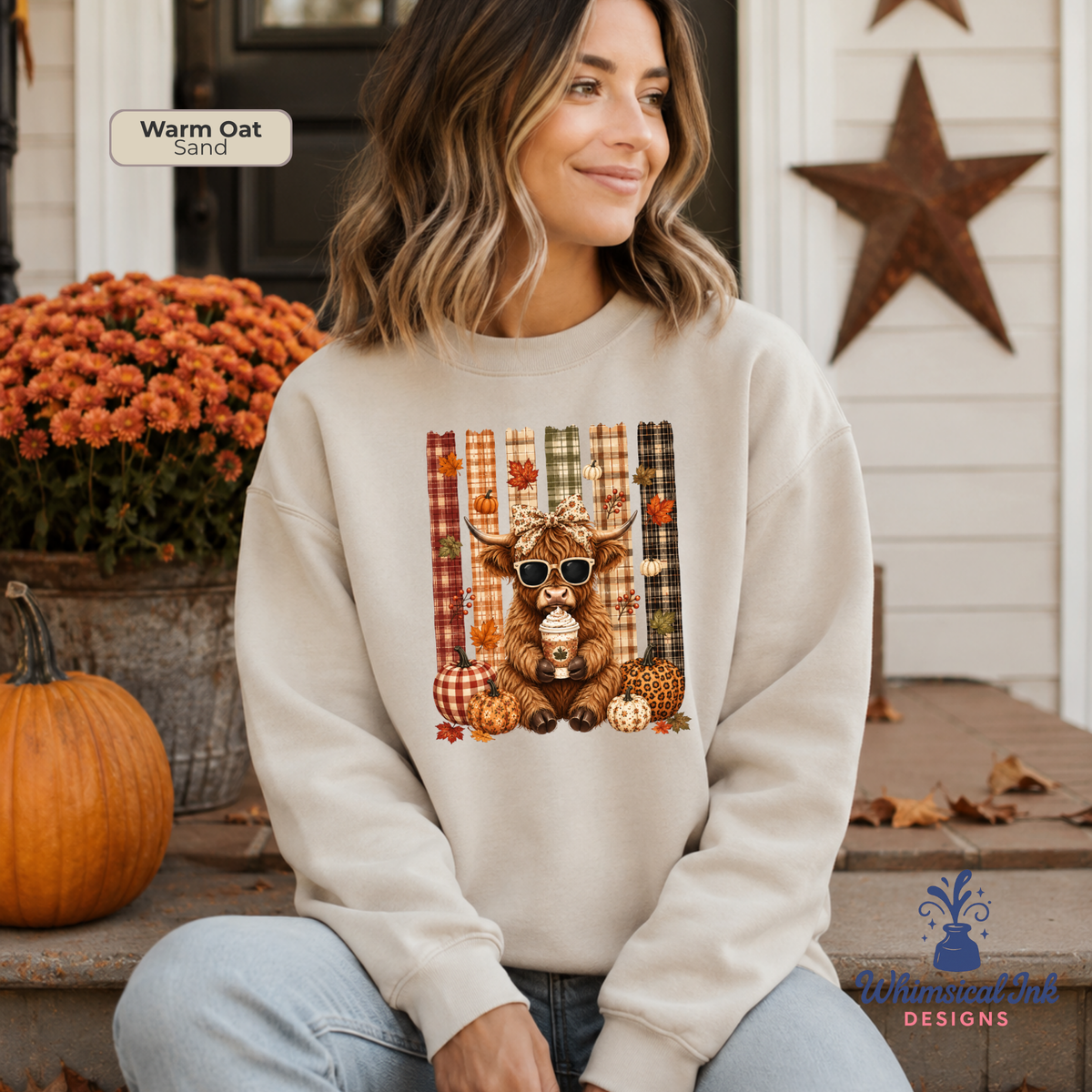 A woman wearing a cream-colored sweatshirt with a fall-themed graphic of a highland cow wearing sunglasses, sitting on a porch with pumpkins and orange flowers in the background.