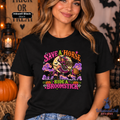 A woman wearing a black graphic t-shirt with a colorful 'Save a Horse, Ride a Broomstick' Halloween design, posed in a cozy, decorated autumn setting with pumpkins and lanterns.