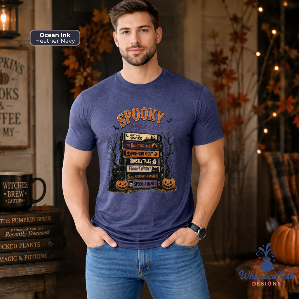 A man wearing a heather navy blue graphic t-shirt with a 'Spooky Stack' of books and pumpkins, standing in a rustic, Halloween-themed room with autumn decorations.