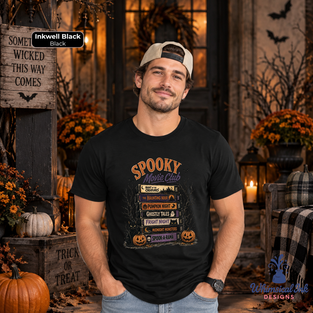 A man wearing a black graphic t-shirt with a 'Spooky Movie Club' theme, posed in a Halloween-themed rustic room setting with pumpkins, autumn decorations, and warm lighting.