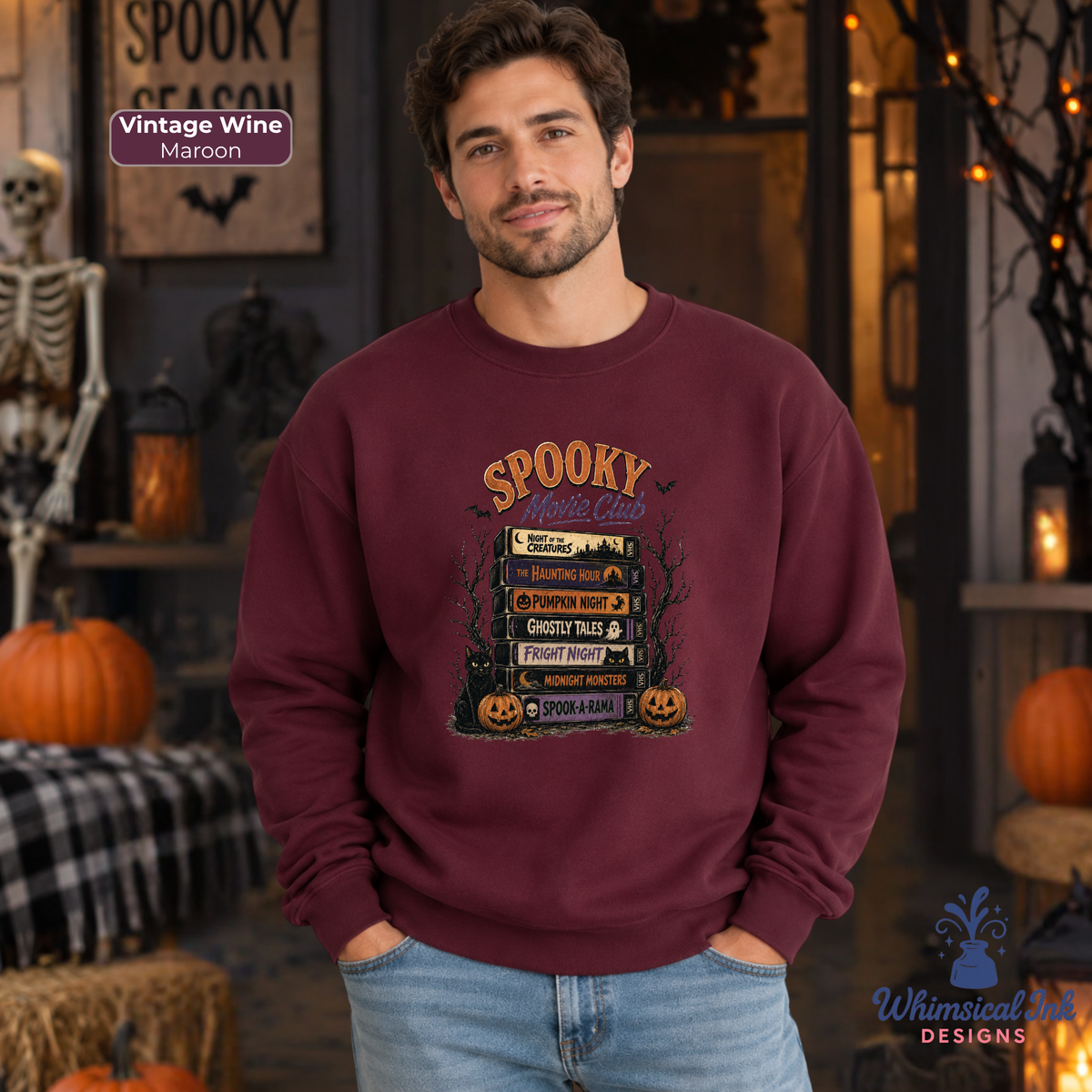 A man wearing a maroon crewneck sweatshirt with a 'Spooky Movie Club' graphic, standing in a Halloween-themed room with pumpkins and a skeleton.