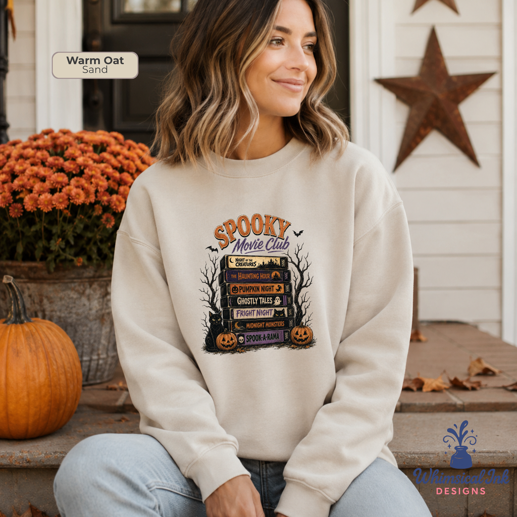 A woman wearing a cream-colored crewneck sweatshirt with a 'Spooky Movie Club' graphic, sitting on a porch with pumpkins and autumn decorations.