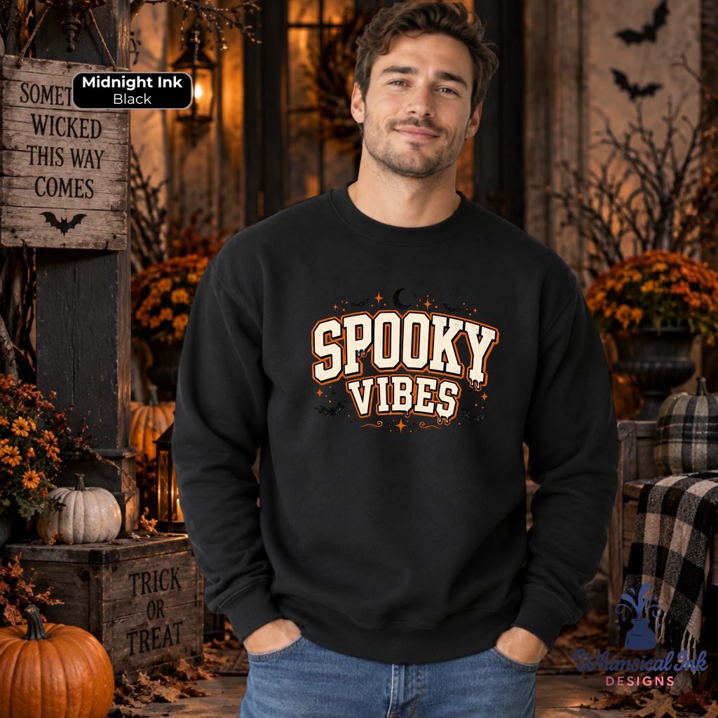 A man wearing a black crewneck sweatshirt with 'Spooky Vibes' printed in cream and orange lettering, posed in a rustic Halloween-themed setting with pumpkins, autumn foliage, and a wooden sign.