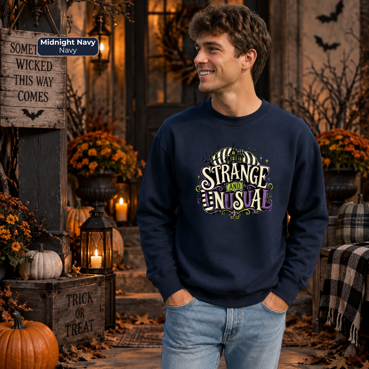 A man wearing a navy-blue crewneck sweatshirt with a 'Strange and Unusual' graphic stand in a Halloween-themed outdoor setting with pumpkins, autumn flowers, and rustic decor.