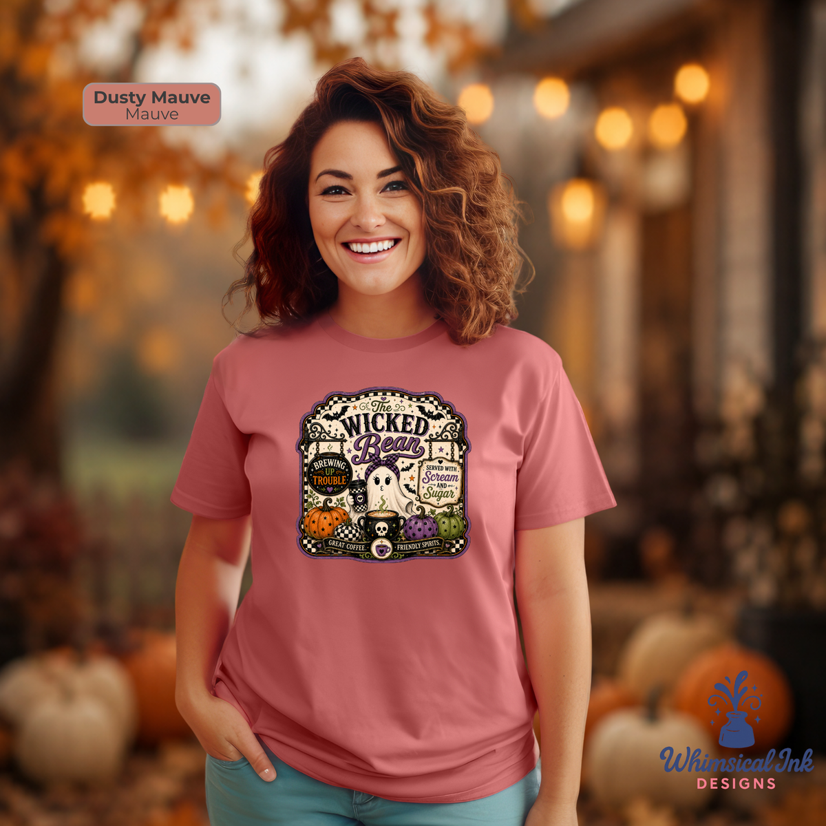 A woman wearing a dusty mauve graphic t-shirt with a Halloween-themed 'Wicked' design, standing in a warm, blurred autumnal setting with pumpkins and string lights. The text 'Dusty Mauve Mauve' is shown in the top left corner, and the 'Whimsical Ink Designs' logo is in the bottom right.