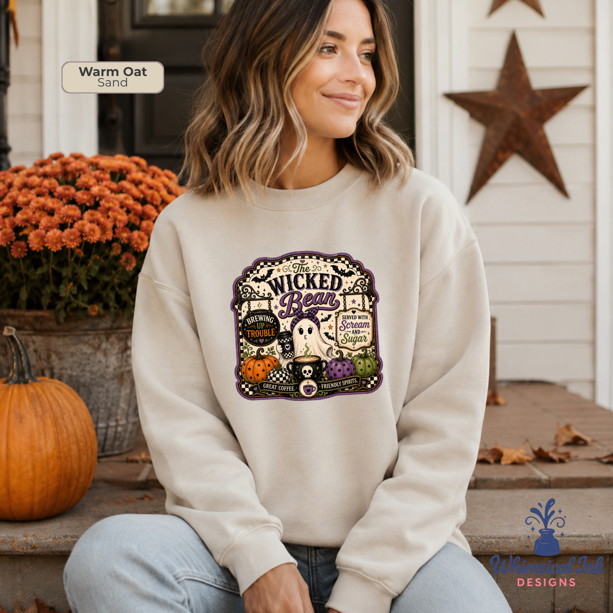 A woman sits on porch steps wearing a cream sweatshirt with a colorful Halloween graphic that reads 'Wicked Beautiful.' The scene includes a pumpkin, orange flowers, a rustic door, and a star decoration.