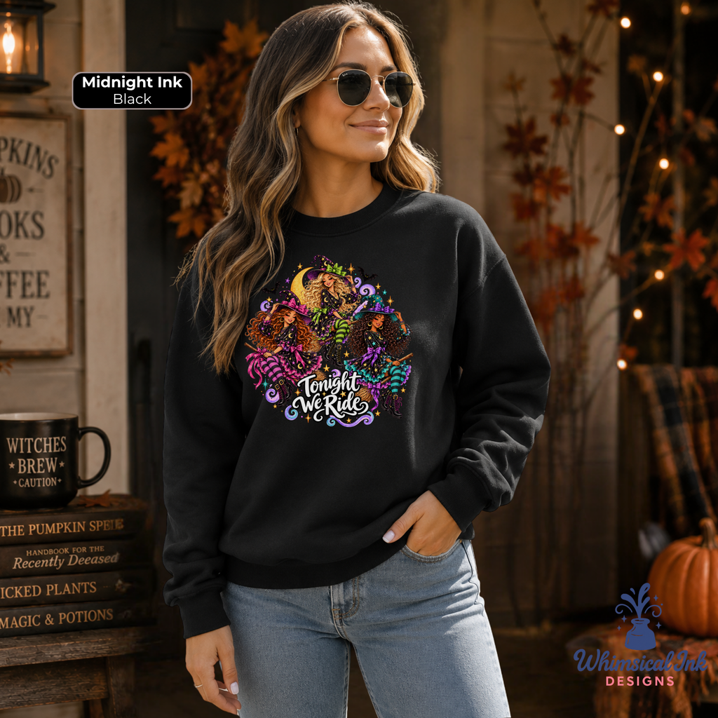 A woman wearing a black crewneck sweatshirt with a colorful graphic of pumpkins, a crescent moon, and the text 'Tonight We Ride' in white script. The background is a cozy, autumn-themed rustic shop setting with fall decorations, a pumpkin, and a sign that reads 'Midnight Ink Black'.