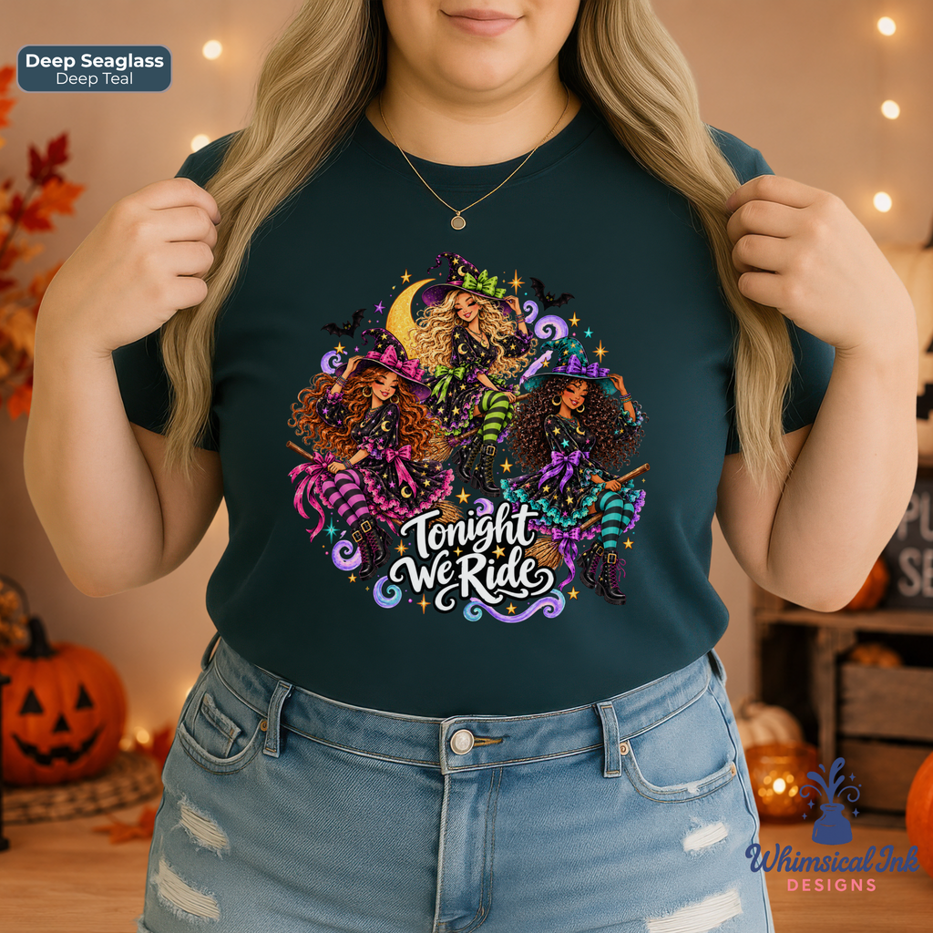 A woman wearing a dark teal graphic t-shirt with a colorful Halloween-themed design featuring three witches, cauldrons, and the text 'Tonight We Ride'. The background is a cozy, warm-toned indoor setting with pumpkins and string lights.