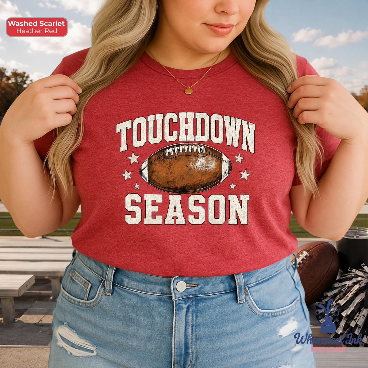 A woman wearing a washed scarlet red graphic t-shirt with 'TOUCHDOWN SEASON' and a football graphic printed on the front, paired with blue jeans in an outdoor setting.